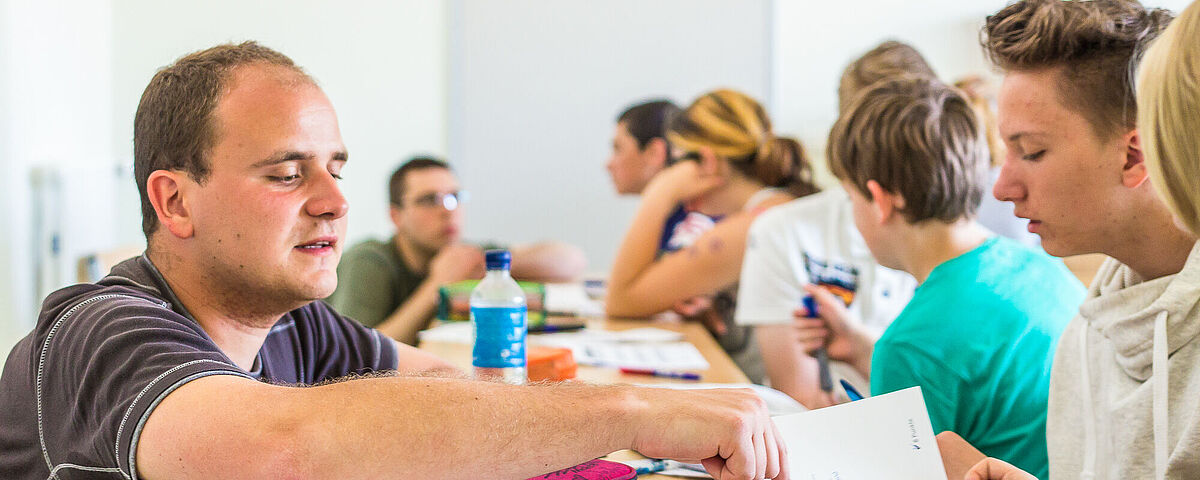 Ein Lehrer erklärt einem Schüler in einer Klasse eine Aufgabe.