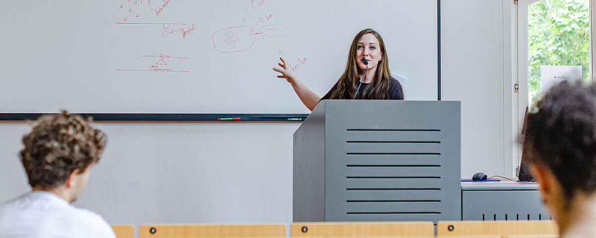 Symbolbild Vorlesung: Eine Dozierende steht vor einem Whiteboard.