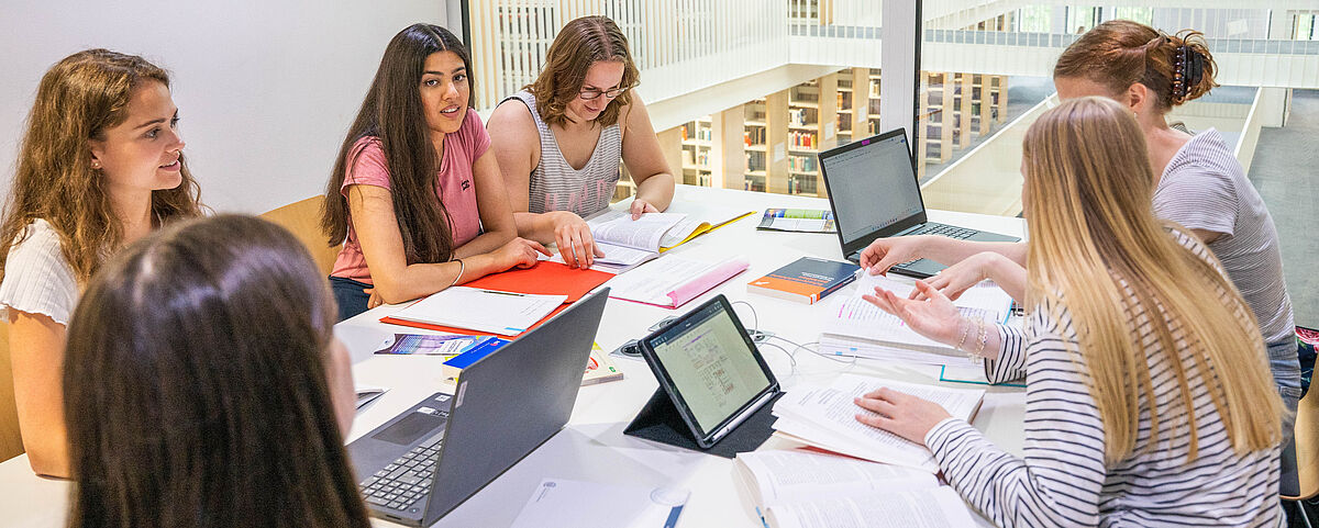 Eine Gruppe von sechs Studentinnen sitzt in einem hellen Gruppen-Carell in der Bibliothek und tauscht sich aus.